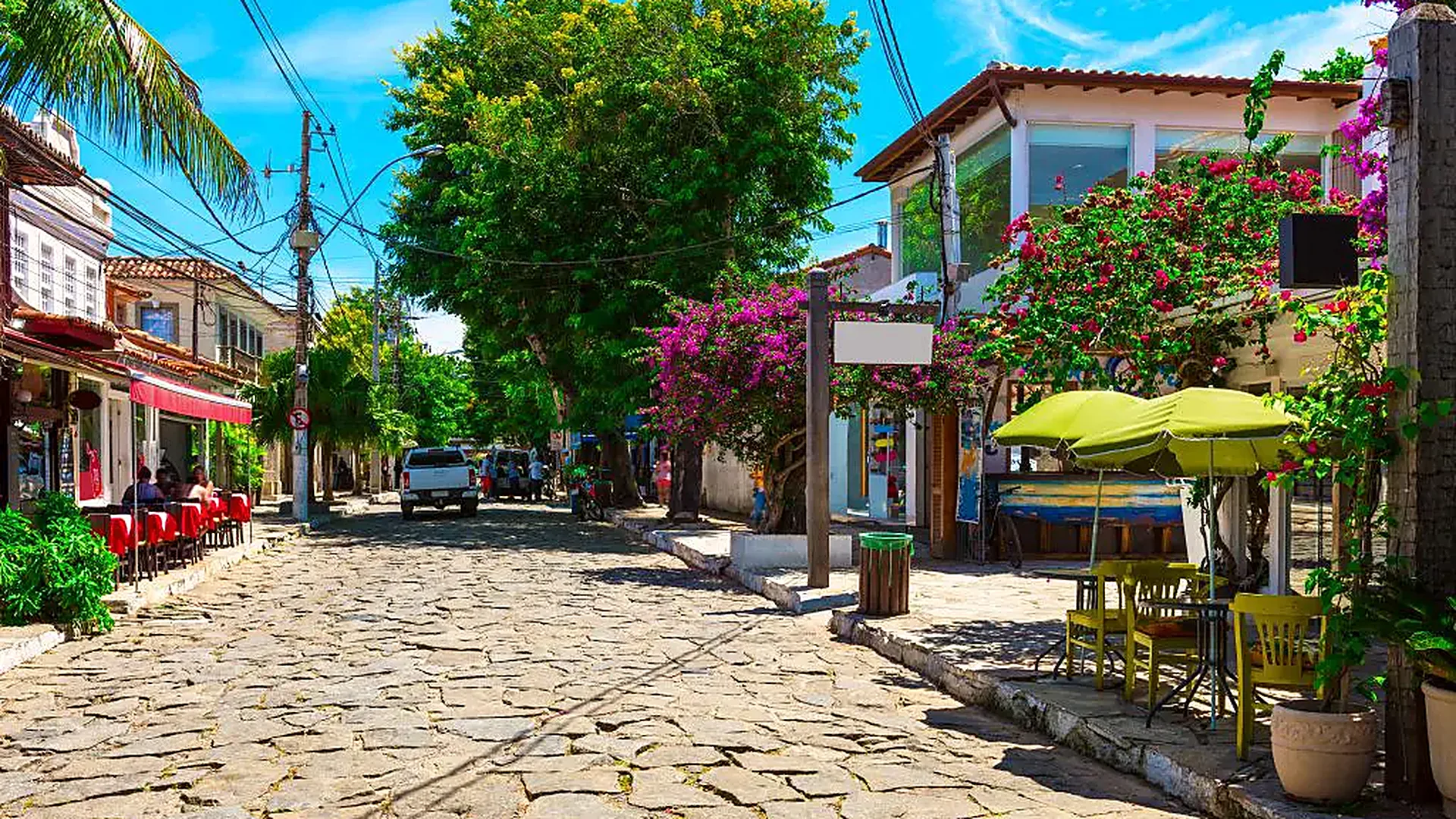Rua das Pedras, em Búzios, com calçamento de pedras portuguesas, buganvílias floridas e fachadas de restaurantes e lojas dos dois lados.