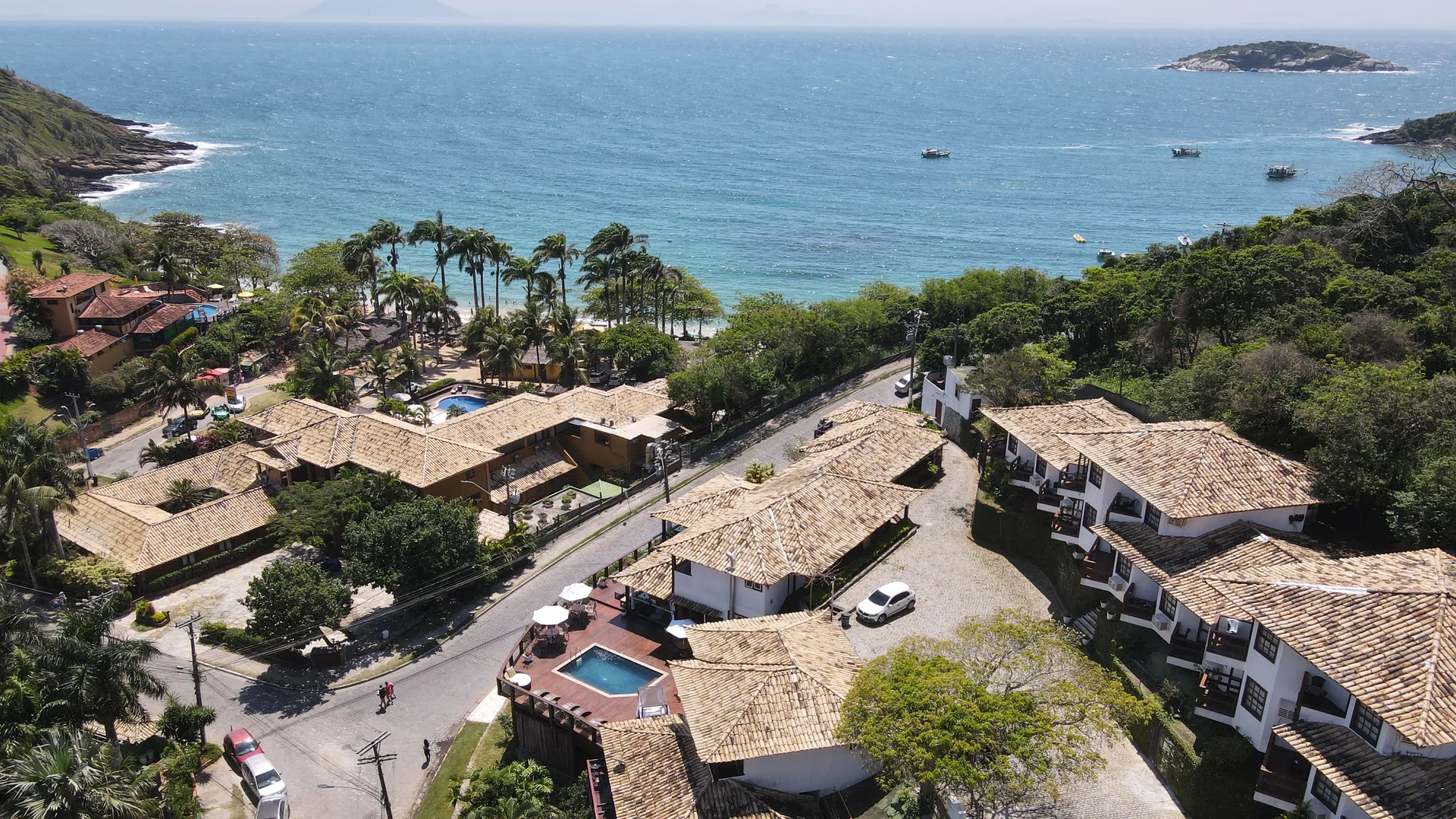 Vista aérea de Armação dos Búzios com casas de telhados coloniais, coqueiros e o mar azul da Praia de João Fernandes ao fundo